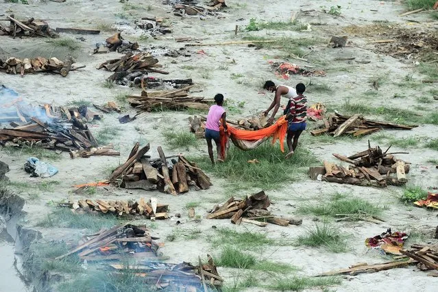 Municipal corporation workers prepare to cremate a body buried in a shallow grave on the banks of the Ganges river during the Covid-19 pandemic as they cremate other bodies also buried there to prevent them from floating downstream as water levels increase near Phaphamau Ghat, in Allahabad on June 25, 2021. (Photo by Sanjay Kanojia/AFP Photo)