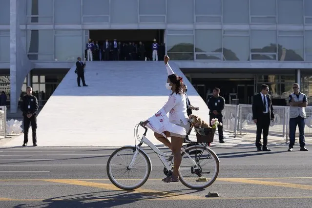 A protester wears clothing stained with fake blood, a reference to COVID-19 deaths, and raises her fist outside Planalto presidential palace where a military convoy passed shortly after in Brasilia, Brazil, Tuesday, August 10, 2021. (Photo by Eraldo Peres/AP Photo)