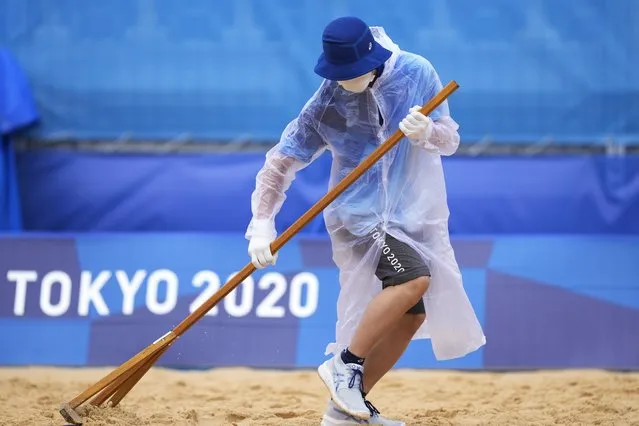 A member of the grounds crew rakes the sand before a men's beach volleyball match at the 2020 Summer Olympics, Tuesday, July 27, 2021, in Tokyo, Japan. (Photo by Petros Giannakouris/AP Photo)