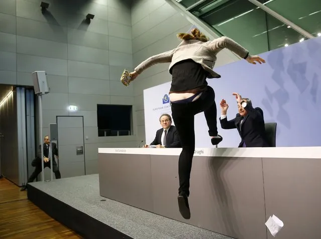 A protester jumps on the table in front of the European Central Bank President Mario Draghi during a news conference in Frankfurt, April 15, 2015. The news conference was disrupted on Wednesday when a woman in a black T-shirt jumped on the podium. (Photo by Kai Pfaffenbach/Reuters)