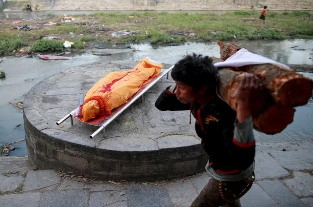 A labourer carrying wood walks past the wrapped body of a victim of Saturday's earthquake before its cremation along a river in Kathmandu, Nepal, April 27, 2015. (Photo by Danish Siddiqui/Reuters)