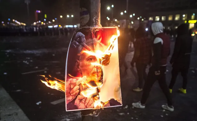 Masked protesters pass a burning poster during a protest rally in front of government headquarters in Bucharest, Romania, early February 2, 2017. Up to 100,000 people gathered peacefully in front of the government building and blocked the city traffic to protest against a government bill, that passed through during a government session on the evening of on Jan. 31, 2017, as a government ordinance to pardon those sentenced to jail terms shorter than five years. According to media reports, the protests took a violent turn when a few hundred allegedly soccer supporters provoked riot police with stones, flares and firecrackers, to which the riot police responded with tear gas and arrests. (Photo by Alex Dobre/EPA)
