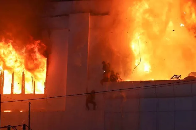 Fire burns around people on a ledge on the side of the Grand Diamond City hotel-casino in Poipet on December 29, 2022. As many as 10 people have died in a fire at a Cambodian hotel-casino on the border of Thailand, with photos showing groups desperately huddled on ledges as fierce flames surround them. (Photo by AFP Photo/Stringer)