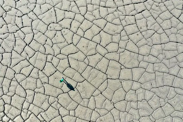 An aerial picture shows a man walking on the dried-up bottom of the Banja hydro-power plant reservoir near Gramsh, central Albania on October 29, 2021. Albania relies entirely on hydro-generated electricity and the uneven pattern of rains in the year makes it dependent on electricity imports. The hike of energy prices in Europe is affecting Albania too with government deciding to step in to support the state-owned enterprises from the budget in order to prevent tariff hikes for households and small businesses. (Photo by Gent Shkullaku/AFP Photo)