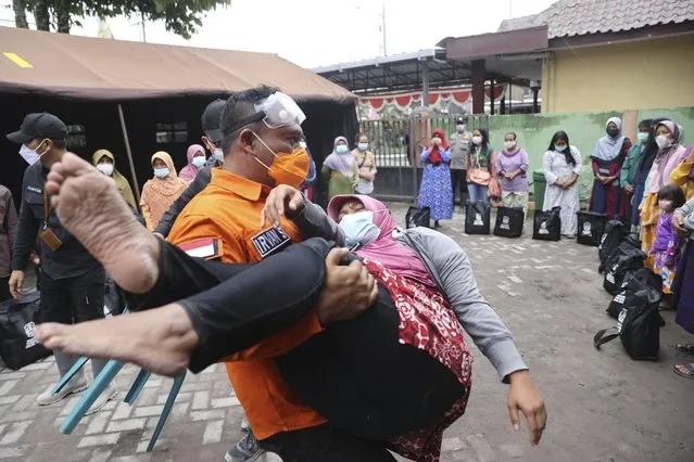A rescuer holds a woman who fell down in a faint, after seeing her house destroyed by the eruption of Mount Semeru in Lumajang district, East Java province, Indonesia, Sunday, December 5, 2021. (Photo by Trisnadi/AP Photo)