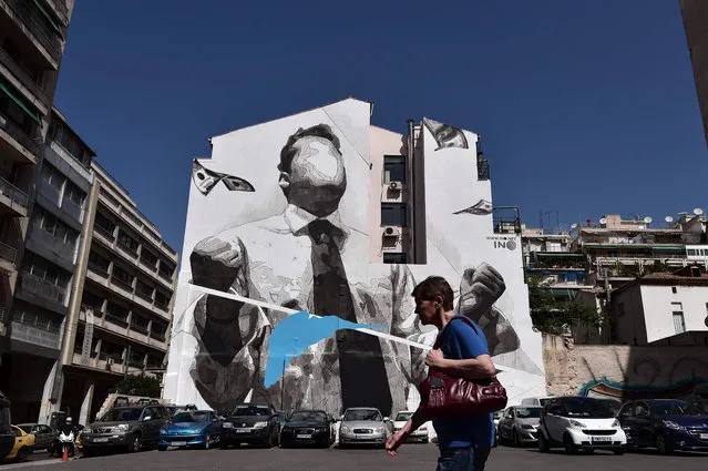 A woman walks past a mural by Greek street artist INO in Athens on April 20, 2016. Talks with EU-IMF creditors continue in Athens on a delayed reforms audit that Greece hopes to conclude by May 1. (Photo by Louisa Gouliamaki/AFP Photo)