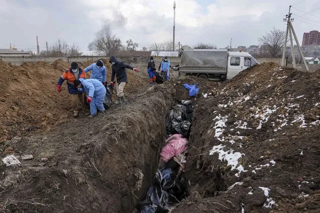 Dead bodies are put into a mass grave on the outskirts of Mariupol, Ukraine, Wednesday, March 9, 2022 as people cannot bury their dead because of the heavy shelling by Russian forces. (Photo by Evgeniy Maloletka/AP Photo)
