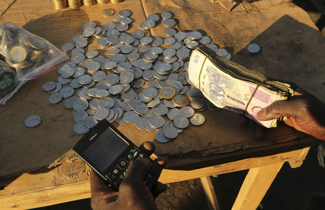 In this photo taken Thursday, August 8, 2019, a vendor transacts on his mobile phone while selling cash in Harare, Zimbabwe. With inflation soaring and cash in short supply, many Zimbabweans transfer funds using their mobile phones and pay a premium to get currency. (Photo by Tsvangirayi Mukwazhi/AP Photo)