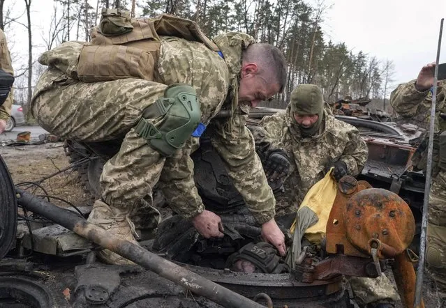 Ukrainian soldiers work to remove the body of a Russian soldier from a destroyed Russian tank, in the village of Dmytrivka close to Kyiv, Ukraine, Saturday, April 2, 2022. At least ten Russian tanks were destroyed in the fighting two days ago in Dmytrivka. (Photo by Efrem Lukatsky/AP Photo)