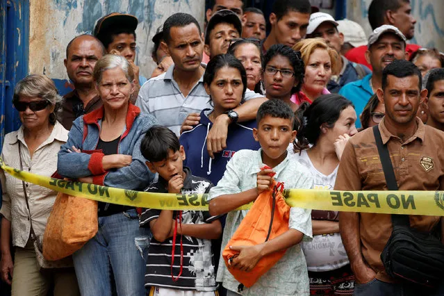 People look at police officers and criminal investigators while they collect evidence in front of a bakery, after it was looted in Caracas, Venezuela April 21, 2017. (Photo by Carlos Garcia Rawlins/Reuters)
