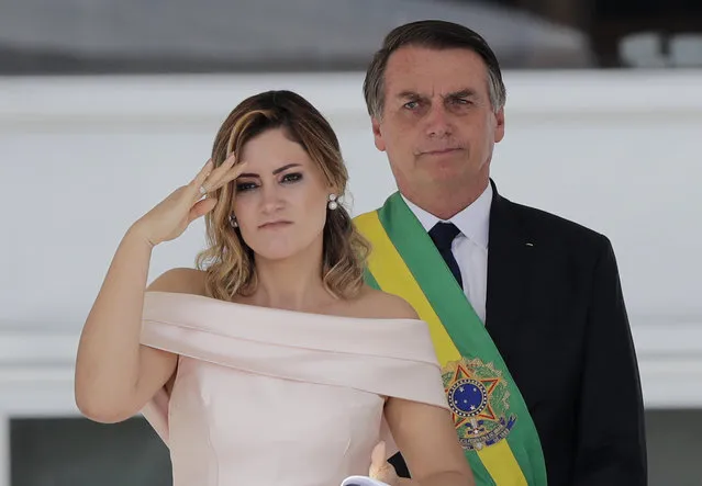 With her husband, Brazil's new President Jair Bolsonaro in the background, Brazil's new first lady Michelle Bolsonaro gives a military salute from the Planalto Presidential palace, in Brasilia, Brazil, Tuesday, January 1, 2019. (Photo by Silvia Izquierdo/AP Photo)