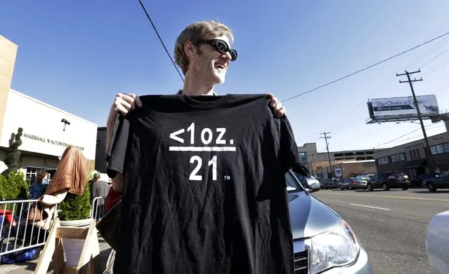 Terry Martin displays a tee shirt he's selling celebrating legal marijuana in front of Cannabis City, as he waits with others on the first day that sales of recreational pot is legal in the state Tuesday, July 8, 2014, in Seattle. The symbols translate that under one ounce of pot and over 21-years of age means that it's legal. The shop is the first and, initially, only store in Seattle to legally sell pot. (Photo by Elaine Thompson/AP Photo)