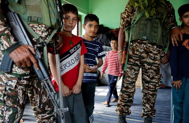 Kashmiri children stand with Indian security personnel inside a polling station, ahead of the second phase of the assembly elections, in Srinagar on September 24, 2024. (Photo by Sharafat Ali/Reuters)