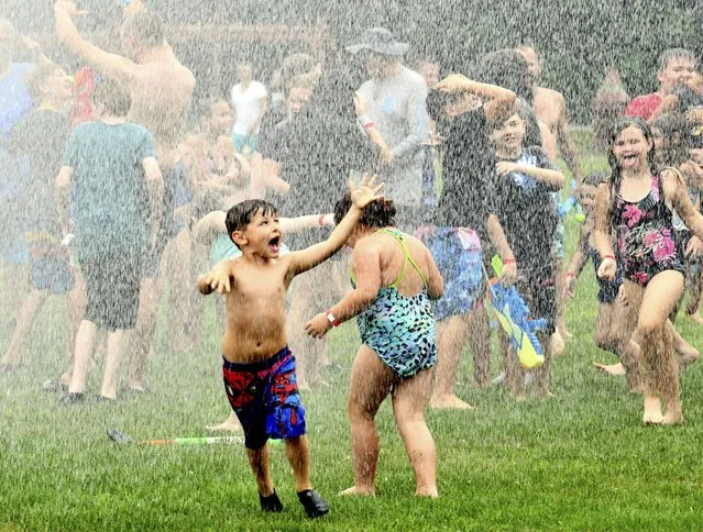 Water rains down on children during the Geneva Water Battle, Sunday, July 24, 2022, at Memorial Field in Geneva, Ohio. Firetrucks provided a cooling opportunity for hundreds of people during the annual event. (Photo by Warren Dillaway/The Star-Beacon via AP Photo)
