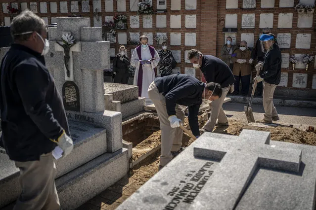 A priest and relatives pray as a victim of the COVID-19 is buried by undertakers at the Almudena cemetery in Madrid, Spain, Saturday March 28, 2020. In Spain, where stay-at-home restrictions have been in place for nearly two weeks, the official number of deaths is increasing daily. (Photo by Olmo Calvo/AP Photo)