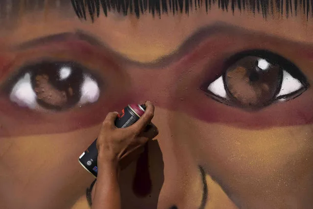 A graffiti artist paints the face of an Indigenous youth after being asked to express on canvas the constitutional right to vote, outside the Supreme Court in Brasilia, Brazil, Tuesday, May 17, 2022. Several artists were asked to interpret a different constitutional right through a painting outside the court. (Photo by Eraldo Peres/AP Photo)