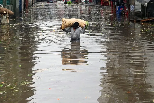 A vendor carries a sack of leafy vegetables wading across a flooded market place after heavy rainfall in Lahore on July 21, 2022. (Photo by Arif Ali/AFP Photo)