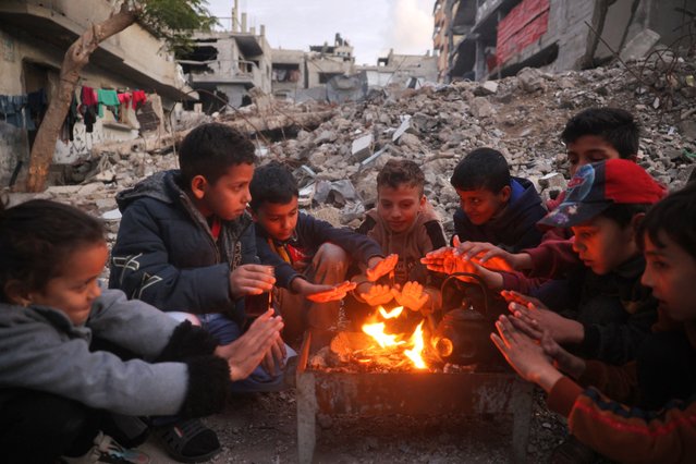 Children warm by the fire at the Bureij camp for displaced Palestinians on December 30, 2024, amid the continuing war between Israel and the militant Hamas group. Since the war between Israel and Hamas began in October last year, Gaza's 2.4 million residents have endured severe shortages of electricity, drinkable water, food and medical services. (Photo by Eyad Baba/AFP Photo)