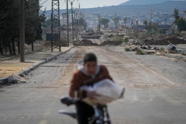 A boy rides his bicycle on a road blocked by Israeli army armoured vehicles in the outskirts of the town of Quneitra, Syria, Sunday January 5, 2025. (Photo by Mosa'ab Elshamy/AP Photo)