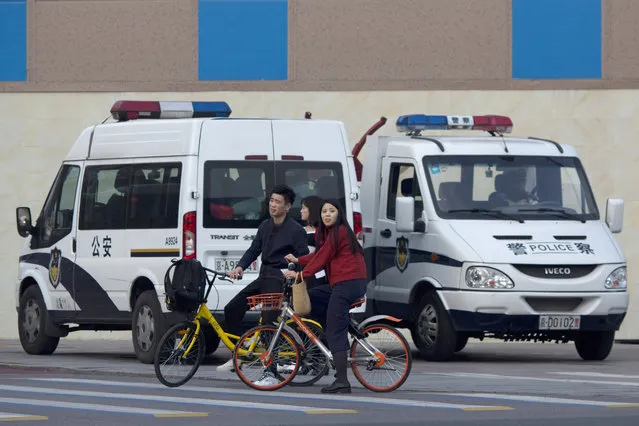 In this October 15, 2017 photo, residents ride bicycles past police van parked at a junction in Beijing, China. (Photo by Ng Han Guan/AP Photo)