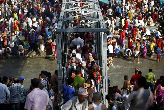 Hindu devotees cross a bridge over Bagmati River to perform religious rituals on the banks of the river while celebrating Kuse Aunse (Father's Day) at Gokarna Temple in Kathmandu, Nepal September 13, 2015. (Photo by Navesh Chitrakar/Reuters)