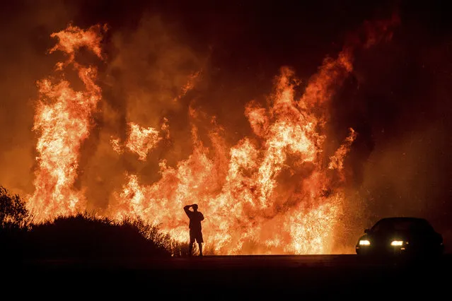 A motorists on Highway 101 watches flames from the Thomas fire leap above the roadway north of Ventura, Calif., on Wednesday, December 6, 2017.  As many as five fires have closed highways, schools and museums, shut down production of TV series and cast a hazardous haze over the region. About 200,000 people were under evacuation orders. No deaths and only a few injuries were reported. (Photo by Noah Berger/AP Photo)