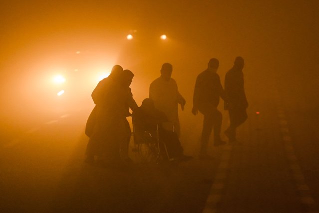 A wheelchair-bound person is assisted by others to cross to a traffic island in the middle of a road in low visibility conditions amdist a massive dust storm in Iraq's southern city of Basra on April 14, 2025. Around 1,500 people were sent to hospitals with respiratory problems on April 14 as a storm hit central and southern Iraq, health officials said. (Photo by Hussein Faleh/AFP Photo)
