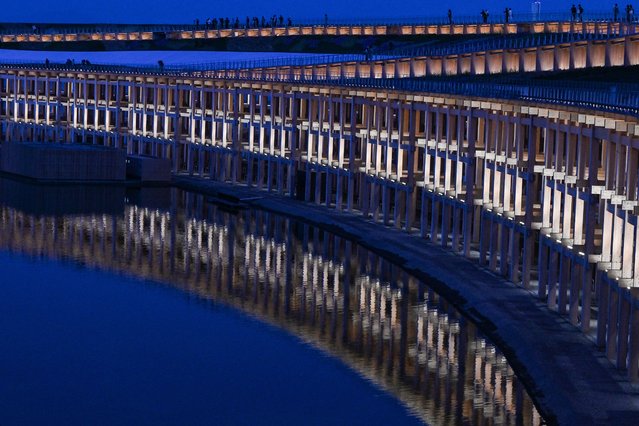Visitors (top) walk along the “Grand Ring”, made of wood, as it is reflected in the water during a media preview day for the 2025 Osaka Expo in Osaka on April 9, 2025, four days before the event opens to the public for six months. (Photo by Richard A. Brooks/AFP Photo)