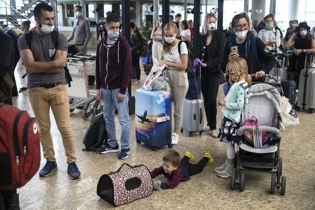 A child plays with a pet as people wait in line to check-in at Sheremetyevo international airport, outside Moscow, Russia, Saturday, August 1, 2020. Russia restarts international flights to Britain, Turkey and Tanzania on Aug. 1 more than four months after closing its borders due to the coronavirus pandemic. (Photo by Pavel Golovkin/AP Photo)