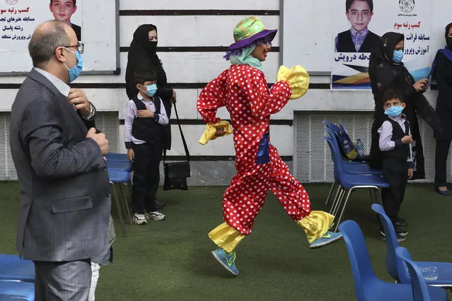 A clown performs as students and their parents wearing protective face masks to help prevent spread of the coronavirus attend the opening ceremony of the Hashtroudi school, in Tehran, Iran, Saturday, September 5, 2020. Iran on Saturday opened the new school year after nearly seven months of closure as many expressed concern over a possible increase in infections of the Covid-19. (Photo by Vahid Salemi/AP Photo)