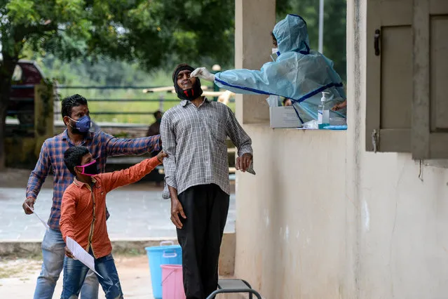 Residents hold a man as a health worker (R) collects a swab sample from him to test for the Covid-19 coronavirus at a community gym centre on the outskirts of Hyderabad on October 8, 2020. (Photo by Noah Seelam/AFP Photo)