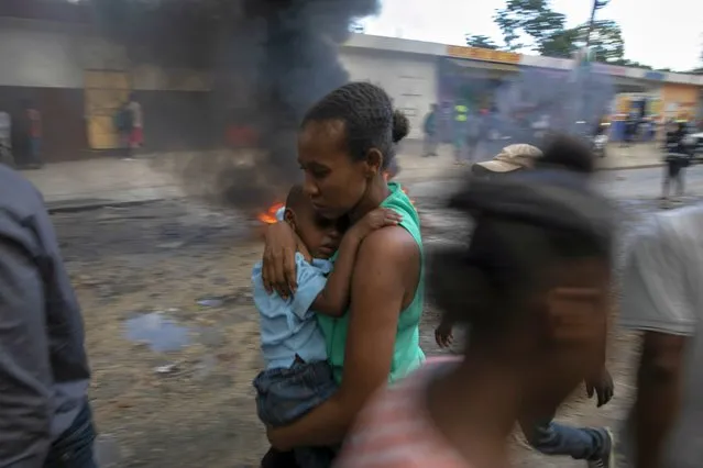 A mother carries her son as she runs past a burning barricade during a protest against the government in Port-au-Prince, Haiti, Friday, November 18, 2022. (Photo by Joseph Odelyn/AP Photo)