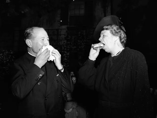 Mrs. Eleanor Roosevelt samples a drum stick of hamburger, corn flakes and egg, cooked by girl scouts over an open fire, during the visit of the First Lady to the National Girl Scout Little House in Washington on October 28, 1941, when she participated in the celebration of National Girl Scout Week. Also shown is The Very Rev. Mgr. Edward Roberts Moore, recipient of a “Thanks Badge” from the Girl Scouts. (Photo by AP Photo)