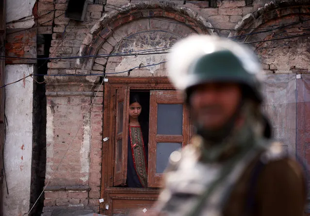 An Indian police officer stands guard as a girl peeps from the window of her house, after Kashmiri separatists called for a day-long strike against the recent killings in Kashmir, in downtown Srinagar April 2, 2018. (Photo by Danish Ismail/Reuters)