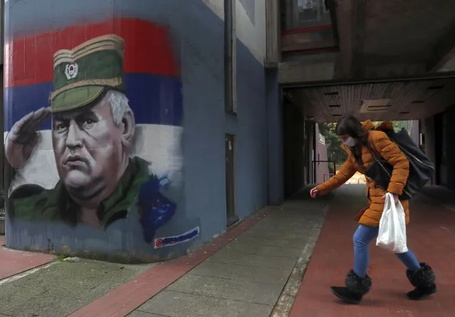 A woman wearing a face mask walks past graffiti depicting former Bosnian Serb wartime general Ratko Mladic in Belgrade, Serbia, Thursday, November 12, 2020. Mladic was convicted by a UN war crimes tribunal in 2017 and sentenced to life imprisonment for masterminding crimes by Bosnian Serb forces throughout the war that left 100,000 dead. (Photo by Darko Vojinovic/AP Photo)
