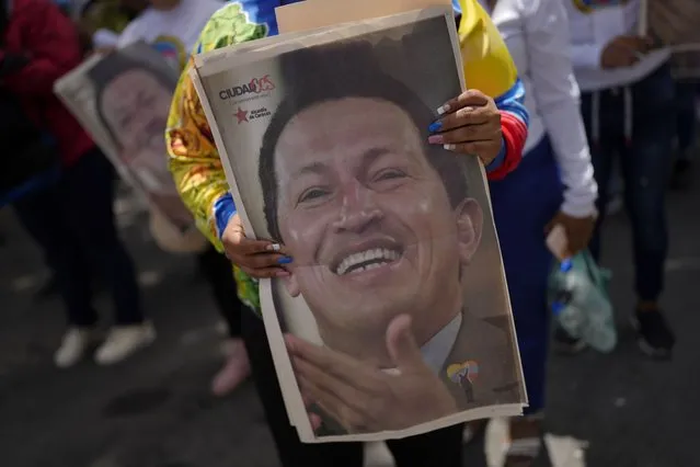 A visitor holds a poster with the image of late Venezuelan President Hugo Chavez as she lines up to visit Chavez's tomb, during commemorations marking the tenth anniversary of his death, at the Cuartel de la Montaña 4F where his remains are interred in Caracas, Venezuela, Sunday, March 5, 2023. Chavez died on March 5, 2013, after a long battle with cancer and chose current president, Nicolas Maduro, a former bus driver and union leader to be his successor. (Photo by Ariana Cubillos/AP Photo)