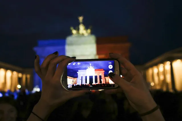 A woman takes a picture of the Brandenburg Gate, illuminated in the French national colors  for the victims killed in the Friday's attacks in Paris, France  in Berlin, Saturday, November 14, 2015. French President Francois Hollande said more than 120 people died Friday night in shootings at Paris cafes, suicide bombings near France's national stadium and a hostage-taking slaughter inside a concert hall. (Photo by Markus Schreiber/AP Photo)