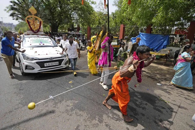 A devotee's cheeks pierced with a metal rod and pulls a car with hooks pierced in his back participates in a religious procession during Panguni Uthiram festival in Ahmedabad, India, Wednesday, April 5, 2023. The festival is observed in the Tamil month of Panguni and is celebrated in honour of the Hindu God Murugan where devotees make offerings to lord Murugan with sacrificial feats they believe will keep them away from evil spirits. (Photo by Ajit Solanki/AP Photo)