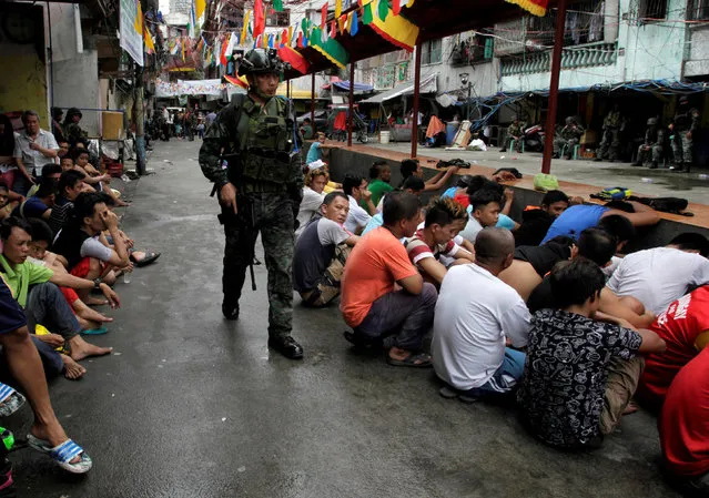 People sit on a street after they were rounded up as they wait to be brought to a police station for verification if they are involved with drugs, after police sources and local media reported that people were killed during a raid, in Manila, Philippines, October 7, 2016. (Photo by Czar Dancel/Reuters)