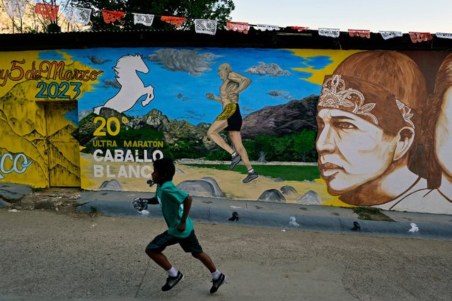 A Raramuri (Tarahumara) runner jogs past a mural during the first day of activities of the ultra marathon Caballo Blanco (White Horse) in Urique, Chihuahua state, Mexico, on March 4, 2023. (Photo by Pedro Pardo/AFP Photo)