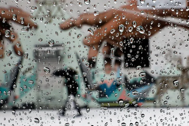 A man with an umbrella is seen through rain drops on a car window walking by a mural in Brooklyn, New York, U.S., February 7, 2018. (Photo by Shannon Stapleton/Reuters)