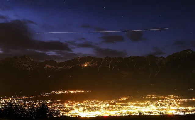 An airplane leaves a light trail as it flies over the snow covered mountain summits of Nordkette mountains behind the city of Innsbruck October 12, 2014. Picture taken using long exposure. (Photo by Dominic Ebenbichler/Reuters)