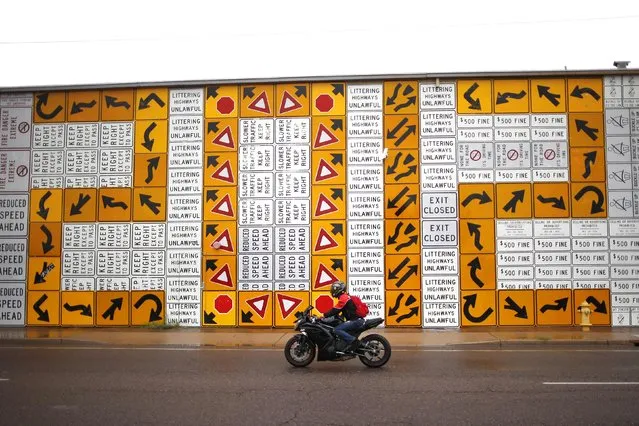A man on a motorbike rides past a mural made from more than 500 highway signs in Phoenix, Arizona January 31, 2015. The mural was created by artist Michael Levine and others in honor of Arizona's centennial in 2012. (Photo by Lucy Nicholson/Reuters)