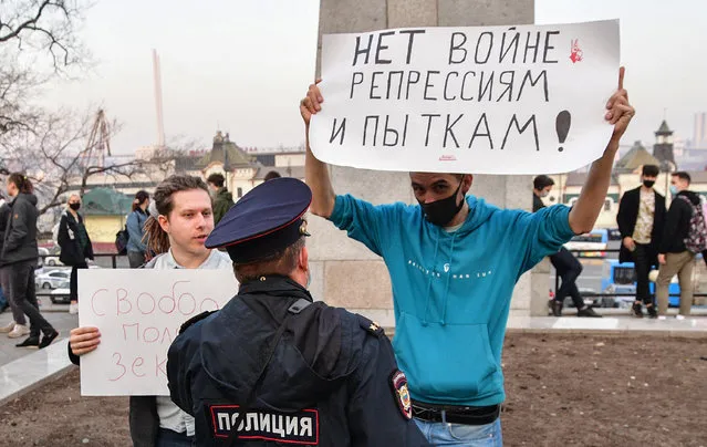 A Russian police officer speaks with an opposition supporter holding a poster reading “No war, repressions and tortures!” during a rally in support of jailed Kremlin critic Alexei Navalny in Vladivostok on April 21, 2021. Navalny's team called for the demonstrations in more than 100 cities, after the opposition figure's doctors said his health was failing following three weeks on hunger strike. (Photo by Pavel Korolyov/AFP Photo)