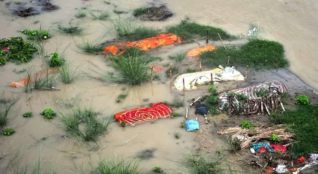 Bodies, many of which are believed to be COVID-19 victims, are seen partially exposed in shallow sand graves as rainwater inundated the site and caused the soil to be washed away at a cremation ground on the banks of the Ganges River on June 28, 2021 in Phaphamau, near Prayagraj (also known as Allahabad), Uttar Pradesh, India. India has seen a steady fall in its COVID-19 infection numbers in June. Many states and cities have made steps towards re-opening fully, though the number of people vaccinated as a share of the overall population remains low and experts raise concerns that re-opening too quickly could once again risk recent gains made in fighting the coronavirus. India also successfully vaccinated up to 8 million people a day in the last week, as the government picks up the pace and announced plans to vaccinate all adults by the end of the year. (Photo by Ritesh Shukla/Getty Images)