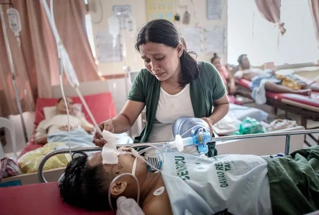 A typhoon victim checks on her husband as she keeps him alive by manualy pumping air into his lungs following his leg amputation that led to an infection, at the Divine Word hospital which still operates without electrical power on the 7th day of the Typhoon Haiyan disaster in Tacloban, on the eastern island of Leyte on November 15, 2013. The United Nations has confirmed at least 4,500 killed in the disaster, which brought five-metre (16-foot) waves to Tacloban, flattening nearly everything in their path as they swept hundreds of metres across the low-lying land. (Photo by Philippe Lopez/AFP Photo)