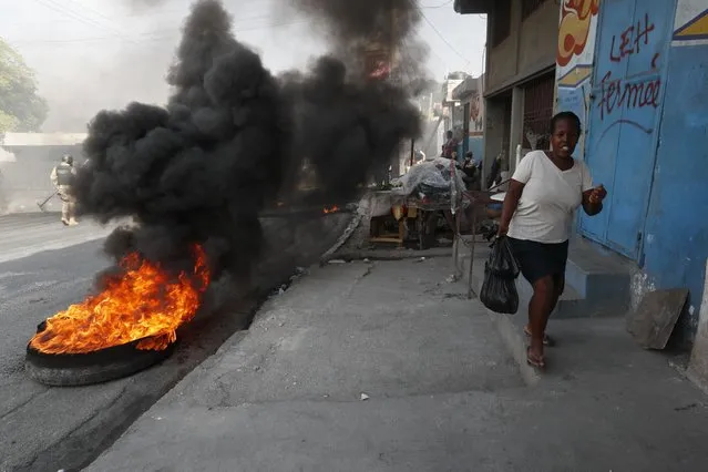 A woman runs past tires set on fire by protesters upset with growing violence in the Lalue neighborhood of Port-au-Prince, Haiti, Wednesday, July 14, 2021. (Photo by Fernando Llano/AP Photo)