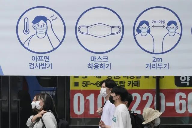 People wearing face masks pass by a banner displaying precautions against the coronavirus on a street in Seoul, South Korea, Friday, August 20, 2021. South Korea's daily increase in coronavirus infections on Friday exceeded 2,000 for the second straight day as officials extended the highest level of social distancing restrictions short of a lockdown in large population centers. The signs read “Get tested if you are sick, left, Wearing a mask, center, and Keep 2 meters away”. (Photo by Ahn Young-joon/AP Photo)