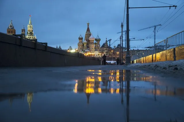 People stay near the place where Russian opposition leader Boris Nemtsov was gunned down one year ago, on February 27, 2015, with St. Basil Cathedral, center, and the Kremlin's Spasskaya, left in the background, in Moscow, Russia, early Saturday, February 27, 2016. (Photo by Pavel Golovkin/AP Photo)