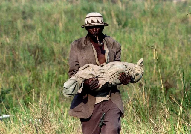 A Rwandan refugee walks through a field on his way to a mass grave carrying the body of his little baby who died of cholera, July 29, 1994. (Photo by Corinne Dufka/Reuters)